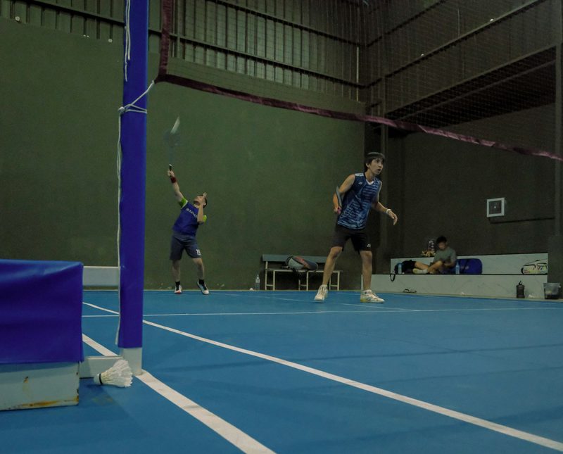 Two people mid-rally on an indoor badminton court.