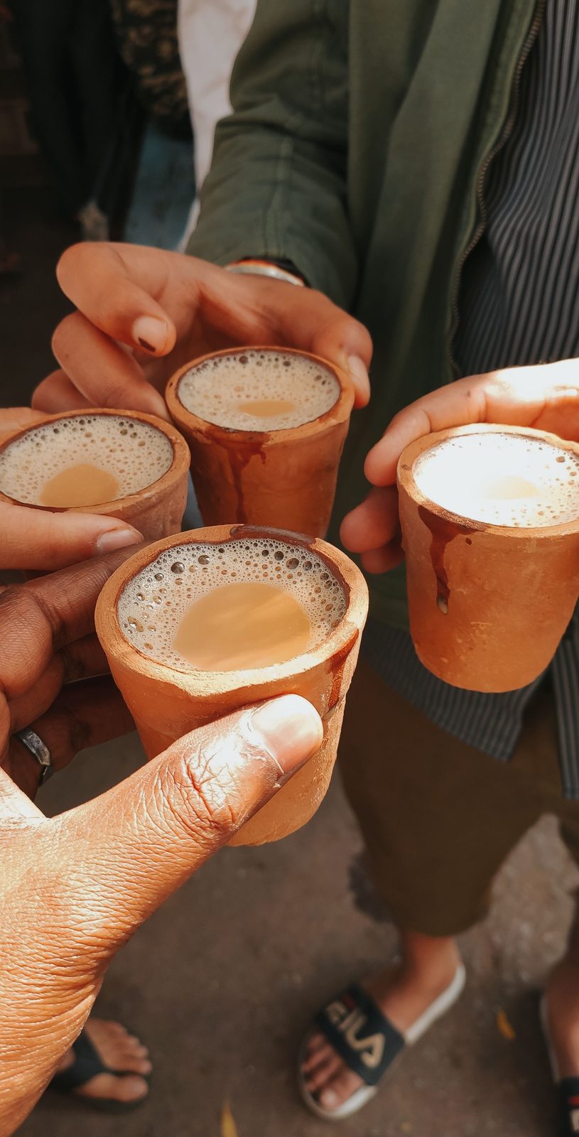 Several hands raising small clay cups of chai together.