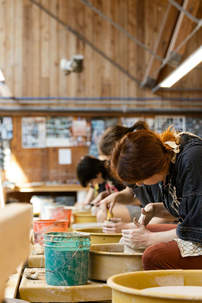 People at a row of pottery wheels in a workshop, shaping clay.