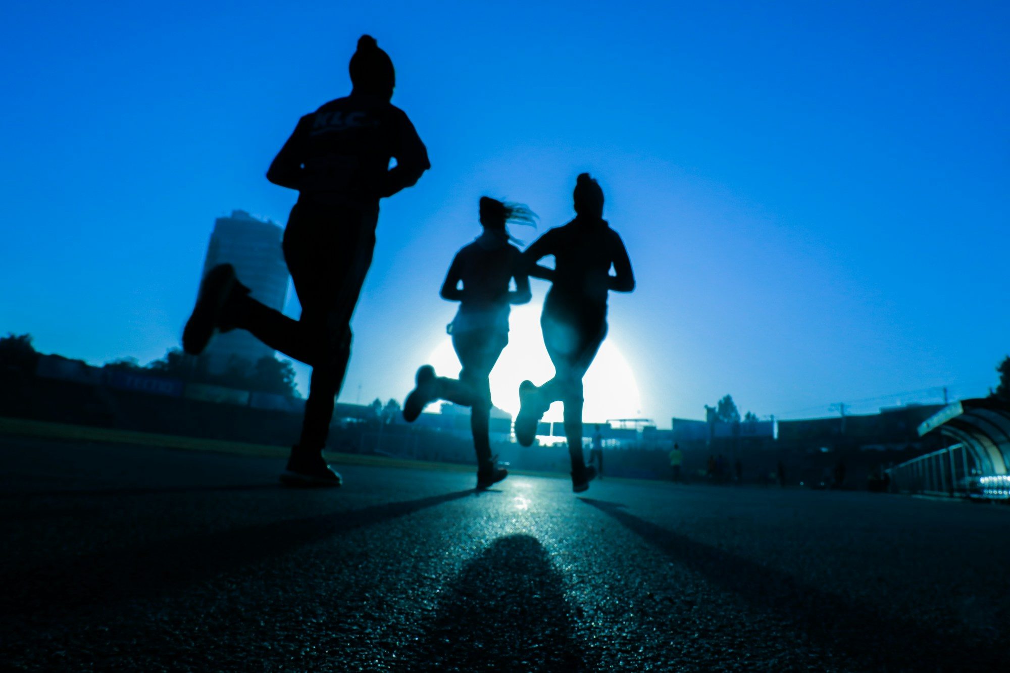 Three runners in silhouette against a bright blue morning sky.